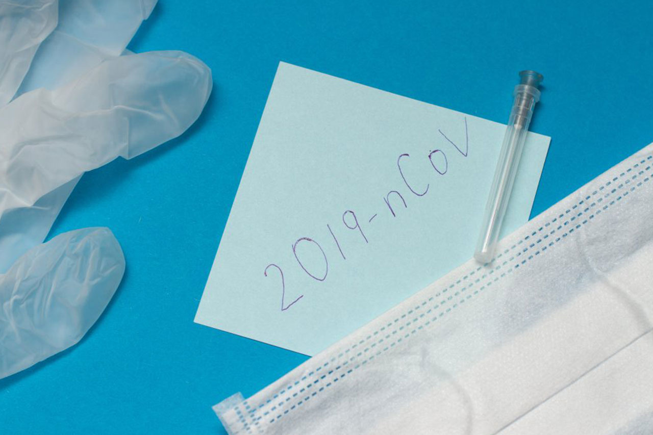 Coronavirus outbreak concept. Novel coronavirus disease called 2019-nCoV handwriting on blue paper. protective mask and surgical gloves on blue background Image credit: Epov / 123rf covid